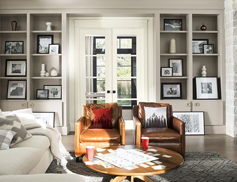 A comfy living room with gray-painted built-in bookshelves, white french doors, a white sofa, and brown leather chairs.